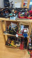 Overview of workbench surface and lower shelf containing assorted power tools, hand tools, cables, and hardware kits.