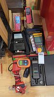Overview of all four devices on wooden surface: CAN OBDII scan tool, impedance meter, insulation tester and tachometer