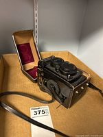 Camera and cases in cardboard tray; camera fitted in half-case with strap, additional brown case open behind