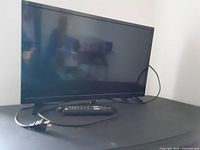 Front view of 24 inch Insignia flat screen TV with remote and stand placed in front, power cord visible