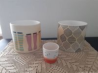 Photo of three ceramic planters: two medium-sized with boot prints and leaf pattern, and one small cactus planter with a white and red gradient and dots.