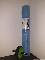 Full view of the medical foam roller wrapped in plastic standing vertically next to the AB roller wheel with black handles and green hubs.