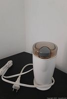 Front angle of coffee bean grinder showing white base, brown lid, gray latch, and wrapped power cord with two-prong plug