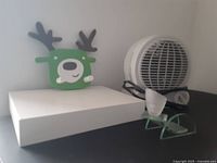 Wide view of heater fan, deer hook on white floating shelf, and frosted glass candle holder in front
