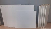 Stack of white Ikea shelving panels including four panels approximately 30" x 10 1/4" and one panel approximately 23" x 24" laid against a wall.