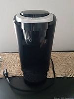 Front view of the black Keurig coffee machine showing the drip tray, power cord, and body shape.