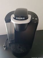 Front view of the black Keurig coffee machine showing water reservoir, drip tray, and power cord.