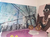 Photo showing Brooklyn Bridge wall art beside Fashion and Glam Oliver wall art with two gold glass candle holders in front.