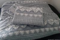 Duvet cover and pillow shams folded on a bed showing gray and white geometric patterns.