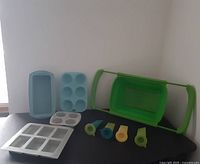 Photo of all silicone bakeware pieces: loaf pan, muffin pan, two gray molds, four colorful ice cream/fruit molds with lids, and green collapsible colander.