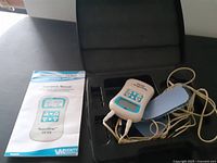 Device, electrode pads with wires, user manual inside black carrying case on black surface