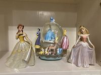 Front view showing all three items: two ceramic princess figurines and the music snow globe with animal and princess figurines