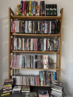 Full view of wooden media stand filled with DVDs, CDs, VHS tapes, Blu-rays, and some stacks of media on floor in front