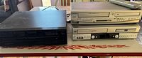 Three devices stacked and side by side: JVC and Sylvania DVD/VCR players, Sony 5-disc CD changer in black.