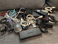 Multiple assorted cables and computer-related devices on couch.