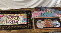 Rubber welcome mat base with Happy Easter insert installed. Additional inserts visible: snowman Welcome, pink floral Welcome, pumpkin trio, blue floral Welcome.