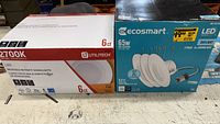Photo of the Utilitech 6-count LED recessed retrofit downlights box and EcoSmart 7-piece LED recessed light kit beside it on a table.
