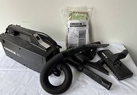 Black Oreck XL handheld vacuum and its accessories laid out on white background, showing main vacuum, hose, nozzle, extension wands, brush, instruction manual and vacuum bags.