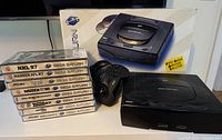 Overview of Sega Saturn console, original box, two controllers and stacked game cases
