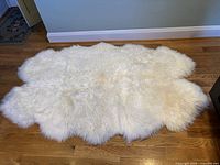 White sheepskin rug laid flat on wooden floor, showing full size and fluffy texture.