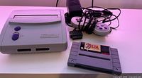 SNES console with Zelda game cartridge and wired controller, power adapter visible in background.