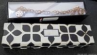 Silver plated chain link bracelet visible through clear top of black and white patterned box
