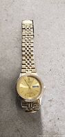 Front view of Citizen gold tone wristwatch showing dial, bezel, and metal bracelet strap on concrete background.