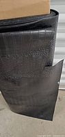 Rolled black crocodile pattern pleather fabric standing upright showing texture and partial edge cuts.