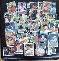Wide view of assorted baseball cards laid out on black surface showing multiple players and team logos.