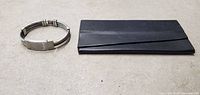 Silver tone bracelet next to black leather card holder on concrete floor