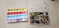 Plastic daily pill box with compartments for morning, noon, evening, and bedtime doses arranged by days of the week alongside a plastic organizer box with assorted buttons and small accessories