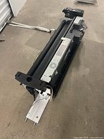 Photo showing the top half of the plotter printer lying on the floor, featuring roller and feed components.