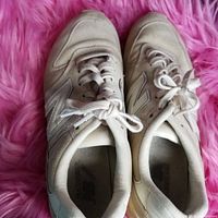 Top view of the pair of gently worn white and beige New Balance sneakers with laces tied, displayed on pink surface.