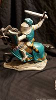 Side view of the ceramic knight riding a black horse with sword raised, showing turquoise armor and gold details.