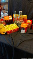 Photo showing assortment of Coca-Cola merchandise including 2 glass bottles, several red and yellow tins, and a metal tray