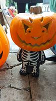 Skeleton figurine wearing black skeleton outfit with removable plastic jack-o-lantern style pumpkin head