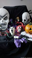 Photo showing a collection of Halloween decorations including two large skull masks, a ghost mask, clown figure, pumpkin decorations, and snake-like prop.