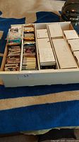 Wide view of large box filled with assorted hockey cards in multiple stacks and protective sleeves along with white storage boxes.