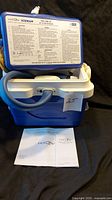 Blue and white Donjoy Iceman Cold Therapy Unit with lid open, visible tubing, and instruction manuals placed in front.