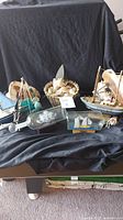 Overall lot display with all boats, ships in bottles, and basket of shells on dark fabric background.
