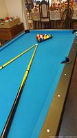 Pool table with blue felt, two small yellow-and-black cues and triangle rack of balls