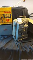 Photo of Kodak Brownie 500 projector with box on black fabric background showing unit and original packaging.