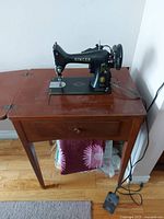 Singer sewing machine on the wooden sewing table, showing sewing machine and drawer with a pink cloth underneath.