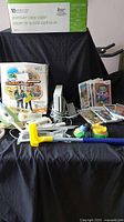 Wide shot showing the Wii console, box for Active Life Extreme Challenge, multiple games in cases, game controllers, and assorted accessories on a dark fabric background.