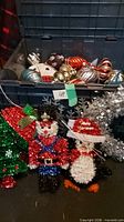 Box containing assorted large Christmas bulbs and glittery outdoor figure ornaments including Santa, penguin, and Christmas tree