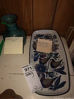 Photo showing the Deichmann pottery vase with label and the Royal Copenhagen ceramic dish with handwritten label indicating Kari Christensen design and item numbers.