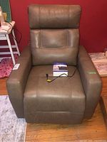 Front view of brown leather electric recliner with power cord and box on seat.