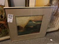 Framed lithograph shown leaning against a wall with visible beige matting and silver frame, bearing a sticker labeled 'Lithograph 910'. The art depicts an abstract geometric composition with muted earth tones.