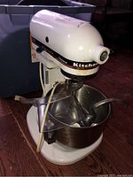 Full view of white KitchenAid Professional stand mixer with stainless steel bowl and plastic splash guard, showing signs of rust on base and body.