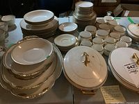 Wide view showing extensive collection including stacks of plates, cups, large serving bowls, and lidded tureens.